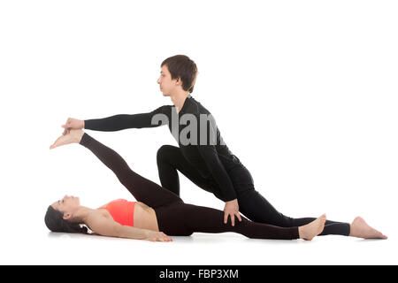 Due sportivi la pratica dello yoga con partner, giovane coaching, aiutando la ragazza per fare reclinabili a mano alluce pongono, supta Foto Stock