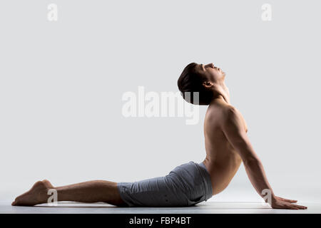Profilo del giovane sportivo uomo che lavora fuori, facendo esercizi per la colonna vertebrale flessibile, bhudjangasana (Bhujangasana o Cobra posa) Foto Stock