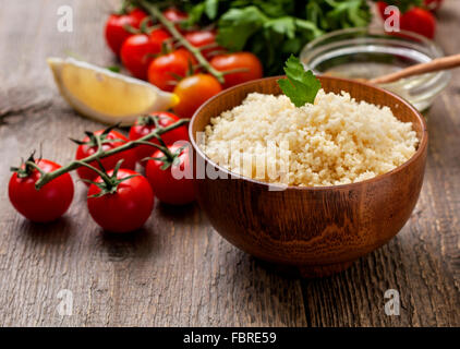 Couscous cotto, verdure fresche per insalata: pomodori, limone, prezzemolo e olio di oliva su un sfondo di legno Foto Stock