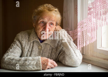 Una donna anziana si siede in una casa vicino alla finestra. Foto Stock