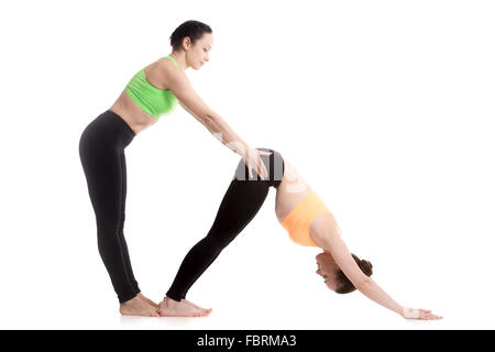 Due belle ragazze sportiva pratica yoga con il partner, coach aiuta a studente, lo stiramento in rivolta verso il basso del cane pongono yoga Foto Stock