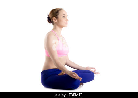 Bella sportiva sorridente ragazza bionda seduta con le gambe incrociate nella variazione di lotus postura, Ardha Padmasana, asana Foto Stock