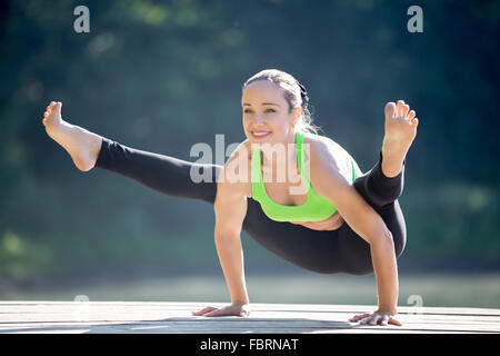 Bella sorridenti sportivo da montare giovane donna bionda in verde sportswear lavorando fuori all'aperto sul giorno di estate, facendo handstand Foto Stock