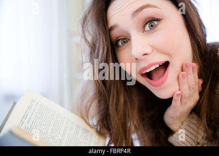 Primo piano della sorpreso piuttosto giovane donna la lettura di un libro a casa Foto Stock