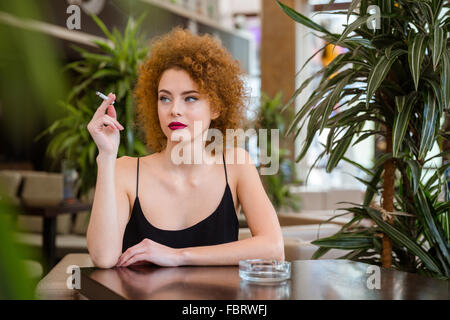 Riflessivo redhead donna con capelli ricci fumare nel ristorante Foto Stock