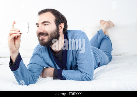 Uomo sorridente con pigiami prendendo un Selfie con uno smartphone Foto Stock