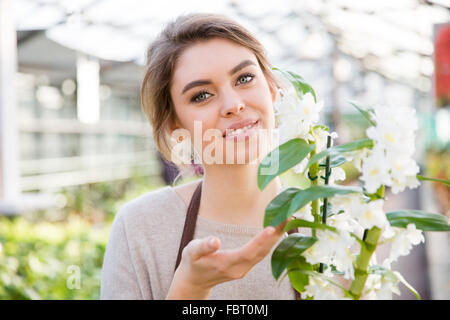 Ritratto di abbastanza felice giovane donna giardiniere con fiore bianco orchid in aranciera Foto Stock