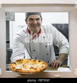 Felice chef offre una pizza fresca attraverso la finestra della cucina. Foto Stock