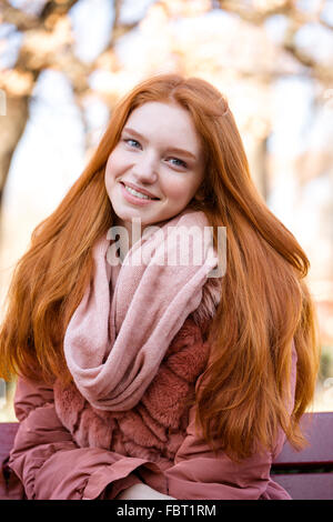 Ritratto di un sorridente redhead donna seduta sul banco di prova all'aperto e guardando la fotocamera Foto Stock