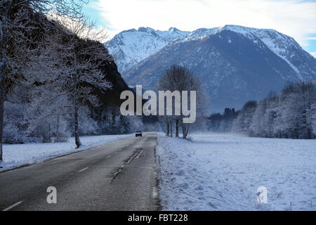 Strada che corre attraverso il paesaggio innevato verso le montagne con auto Foto Stock