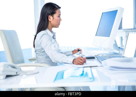 Focalizzato imprenditrice prendere appunti mentre si lavora sul computer Foto Stock