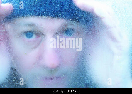 L uomo del peering attraverso un congelati nel riquadro della finestra in inverno Foto Stock