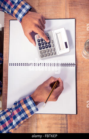 Imprenditore utilizzando la calcolatrice mentre la scrittura sul libro Foto Stock