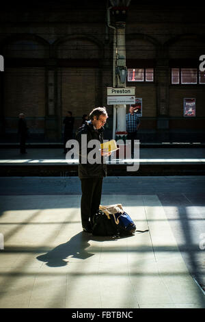 L'uomo assorbiti in un libro in attesa di un treno presso la stazione ferroviaria di Preston e in Lancashire Foto Stock