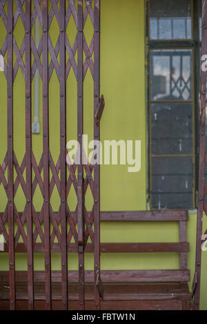 Una sala di attesa. Verde e giallo che mostra a parete mediante un mezzo di chiusura pieghevole in metallo gate. Una panca in legno e finestra dietro. Foto Stock