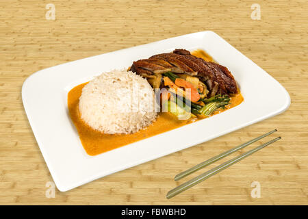 Cucina cinese su una piastra. Anatra arrosto con verdure e riso salsa di cocco. Legno di sfondo con bacchette. Foto Stock