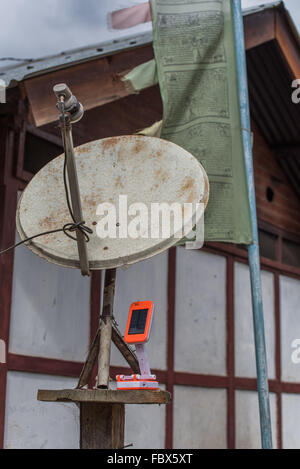 Interessante la giustapposizione di un moderno caricabatterie solare, un arrugginito parabola satellitare e un tradizionale preghiera flag in un remoto villaggio! Foto Stock