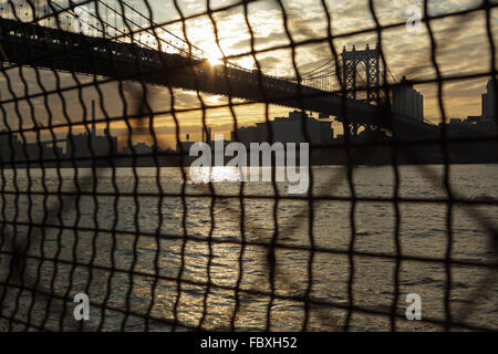 Distorta visione industriale di Manhattan Bridge waterfront sunrise New York City attraverso un recinto di filo Foto Stock