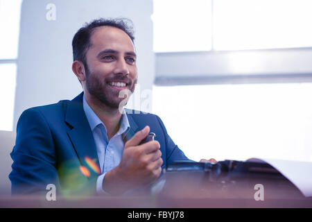 Happy businessman che guarda lontano mentre è seduto in ufficio Foto Stock
