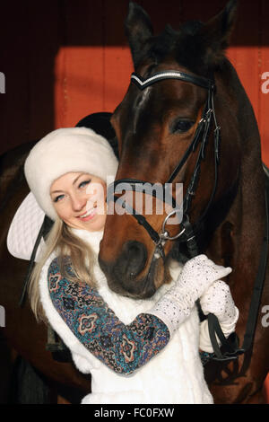 Bella ragazza bionda avvolgente cavallo marrone in inverno agriturismo Foto Stock