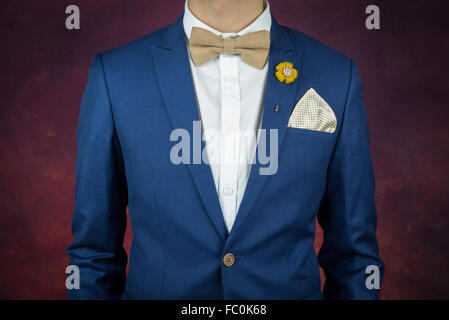 Uomo in tuta blu con crema di caffè bowtie colore, fiore spilla, e la configurazione di punti fazzoletto, close up, regolazione papillon Foto Stock