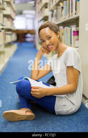 Bellissima femmina studente africano seduto sul pavimento della libreria e la lettura Foto Stock