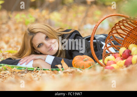 Giovane bella ragazza distesa sulle foglie in autunno la foresta, si trova accanto a un cesto di mele Foto Stock