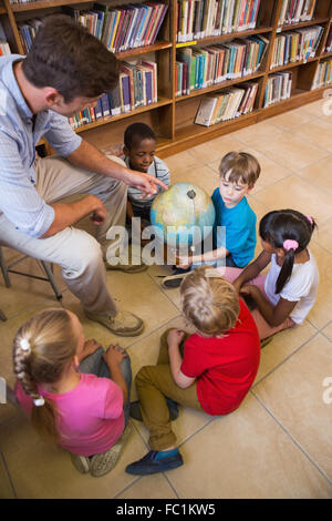 Carino gli alunni e gli insegnanti guardando il globo in biblioteca Foto Stock