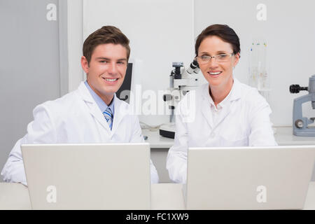 Gli scienziati che lavorano con il computer portatile e sorridente in telecamera Foto Stock