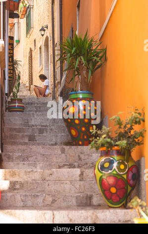 Taormina Sicilia, vista di un giovane seduto a pochi passi che legge un libro in una stradina del centro storico di Taormina, Sicilia. Foto Stock