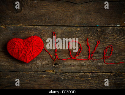 Cuore rosso forma con una iscrizione amore fatti di lana sul vecchio squallido sfondo di legno. Immagine del giorno di San Valentino Foto Stock