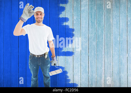 Immagine composita di uomo felice indossando i guanti mentre si tiene il rullo di vernice Foto Stock