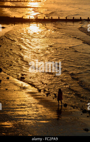 Persona a piedi lungo la spiaggia durante il tramonto CROMER Inghilterra Norfolk Foto Stock