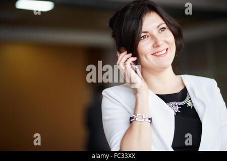 Attraente business donna parlando al telefono, sorriso raggiante, immagine positiva, vestito abito bianco con un severo abito nero. Negoziati, comunicazioni in azienda, copiare lo spazio per il tuo testo. Foto Stock