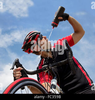 Ciclista bere da una bottiglia mentre in sella a una moto Foto Stock