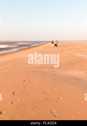 Due giovani donne che assumono una passeggiata serale con il loro cane lungo una spiaggia deserta, lasciando una scia di piedi stampe.Presthaven Sands Foto Stock