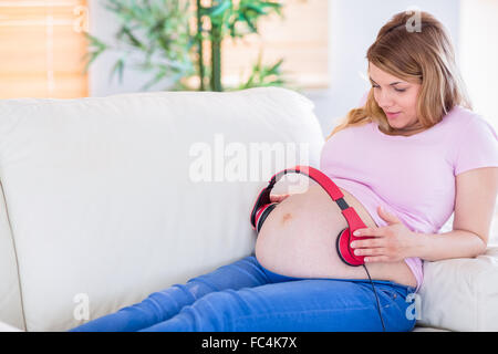 Donna incinta mettendo le cuffie sul suo ventre Foto Stock
