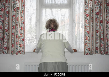 Donna di novanta anni con mano sul radiatore che guarda fuori dalla finestra. REGNO UNITO. Coronavirus, autoisolamento, distanza sociale, quarantena... concetto Foto Stock