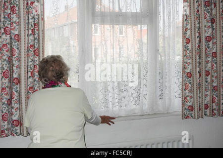 Donna di novanta anni con mano sul radiatore che guarda fuori dalla finestra. REGNO UNITO. Coronavirus, autoisolamento, distanza sociale, quarantena... concetto Foto Stock