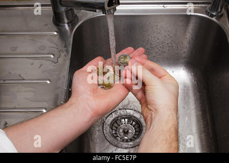 Uomo di monete di lavaggio sotto acqua corrente Foto Stock