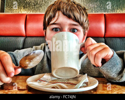 Ragazzo caucasico di bere il caffè in diner Foto Stock