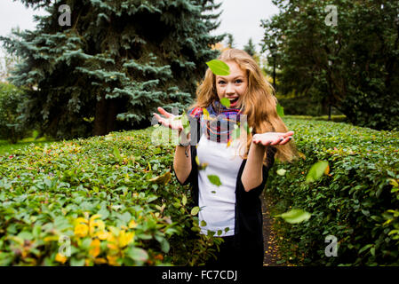 La donna caucasica tossing foglie in giardino Foto Stock