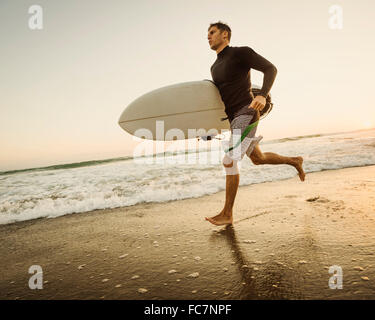 Uomo caucasico che trasportano le tavole da surf in spiaggia Foto Stock