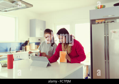 Madre e figlia con tavoletta digitale in cucina Foto Stock