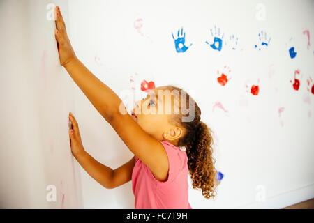 Razza mista ragazza rendendo le stampe a mano sulla parete Foto Stock