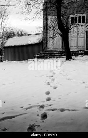 Impostare umana di Orme nella neve conducono verso il comfort di una casa in un paesaggio invernale Foto Stock