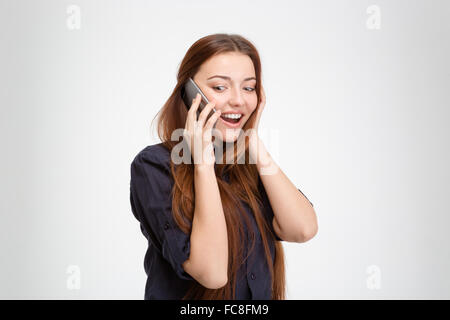 Si chiedeva felice giovane donna in piedi e parlando al telefono cellulare su sfondo bianco Foto Stock