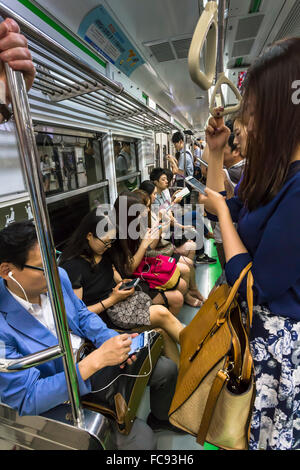 Elegantemente vestito pendolari sulla trafficata alla metropolitana guardando i loro telefoni cellulari e dispositivi, Seoul, Corea del Sud, Asia Foto Stock