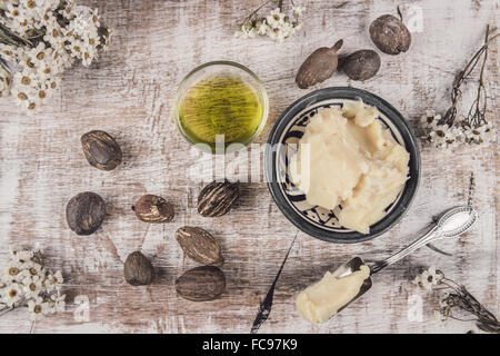 Il burro di karité e l'olio di karité su uno squallido tavolo bianco con fiore bianco e cucchiaio d'argento Foto Stock