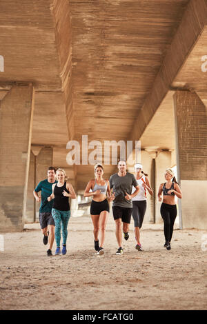 Ritratto di salutare i giovani in esecuzione sotto un ponte. Running Club gruppo di indossare abbigliamento sportivo della formazione in città. Foto Stock